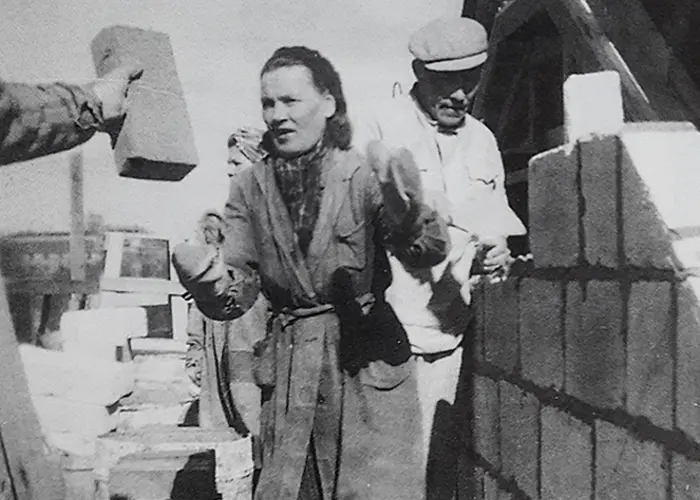 Naisapulainen antaa muurarille tiiliä